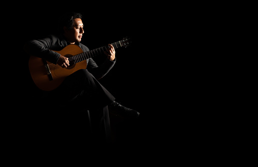 hispanic man playing guitar, guitarist on a black background studio shot, latin professional guitar player