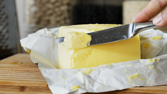 Cropped shot of an unrecognisable woman hand cutting fresh butter with a table knife in home kitchen