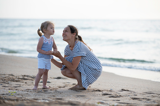 healthy caucasian family sitting mother and jumping high kid on sea shore in autumn sunset