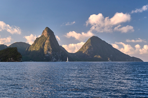 A UNESCO heritage site, the two Pitons of St Lucia, dwarfing a sailboat, are seen from the water at sunrise.