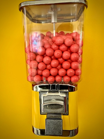 View of a pink chewing gum dispenser on a yellow wall. Photo taken in Montreal in December 2021