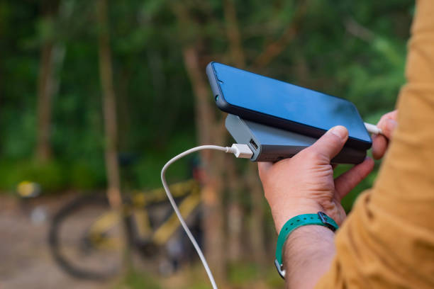 A tourist charges a smartphone with a power bank on the background of a bicycle in forest. A tourist charges a smartphone with a power bank on the background of a bicycle in forest bicycle docking station stock pictures, royalty-free photos & images