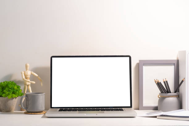 istock Front view of laptop computer with empty display, coffee cup and supplies on white table. 1512507608