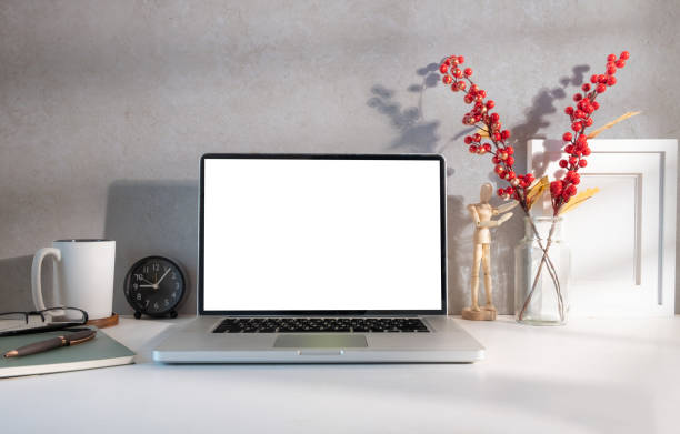 Laptop computer with blank screen, with coffee, books and stationery on white table.