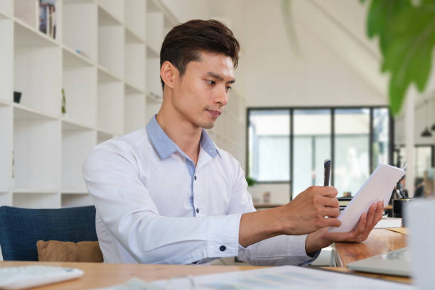 istock Young asian man office worker writing information on notepad, working in modern office. 1512521076