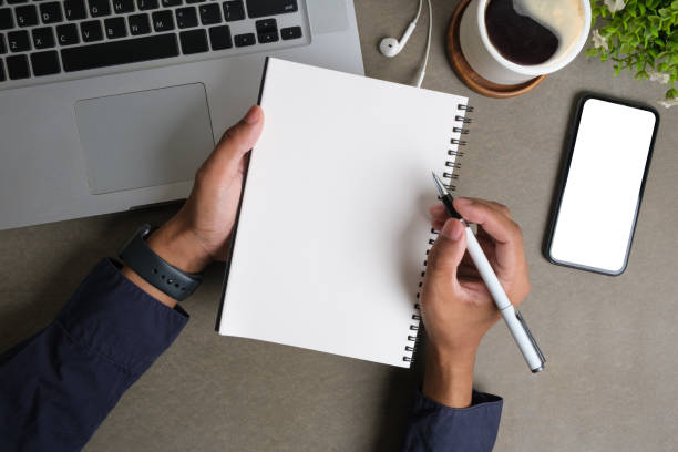 istock Businessman hand holding pen, writing on empty notepad. Above view, blank screen for your advertise design. 1512531730