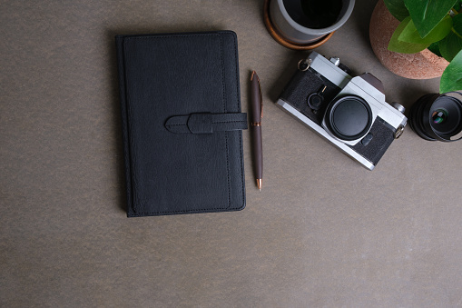 From above view of notebook, retro camera and coffee cup on grey background. Creative workspace.