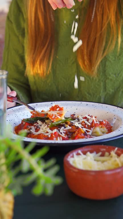 Woman's hand adds, sprinkles grated cheese to Italian pasta with cherry tomatoes at a restaurant.