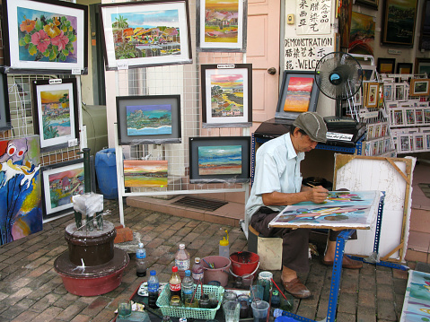January 9, 2009 - Melaka, Malacca State, Malaysia.\nAn elderly male artist at work at the side of the street in Jalan Tokong near to Jonker Walk in the old part of Melaka City, Malacca State, Malaysia with his paintings and painting materials around him.