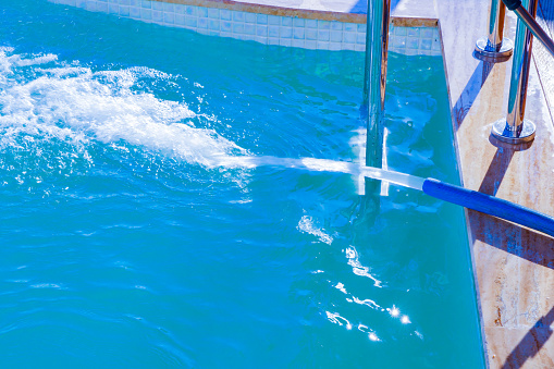 Scene of filling water into swimming pool. Water is filled into the swimming pool with a dark blue water hose. An image that stops the moment.