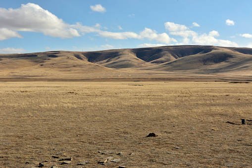 Flat steppe at the foot of a ridge of high hills on a sunny autumn day. Chui steppe, Altai, Siberia, Russia.