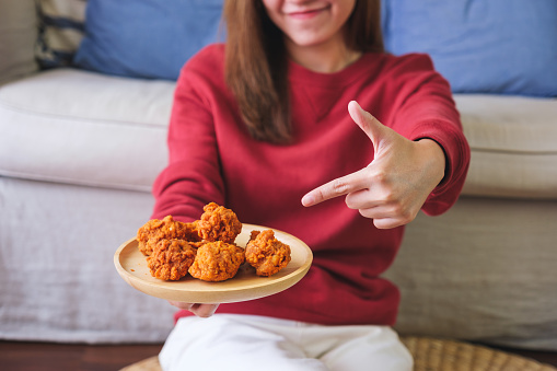 Closeup image of a woman holding and pointing finger at a plate of fried chicken