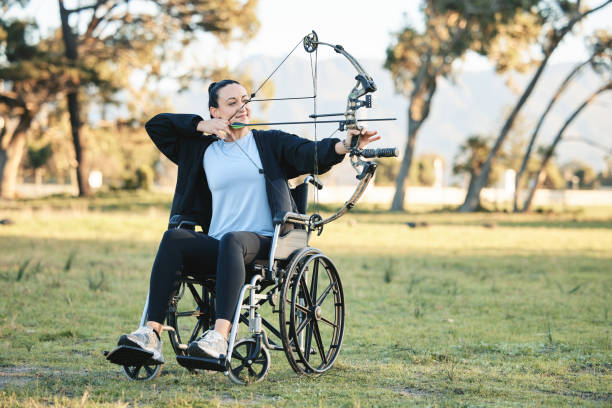 Disabled woman, outdoor archery in wheelchair and challenge with active sports lifestyle in Canada. Person with disability in a park, fitness activity to exercise arms and aim arrow for hobby mujer discapacitada, tiro con arco al aire libre en silla de ruedas y desafío con estilo de vida deportivo activo en canadá. persona con discapacidad en un parque, actividad física para ejercitar los brazos y flecha de puntería para pasatiempo