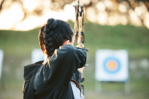 Archer practice, target and bow or arrow training for archery competition, athlete challenge or competitive shooting. Sports field girl, talent or woman focus on precision, aim or back view objective