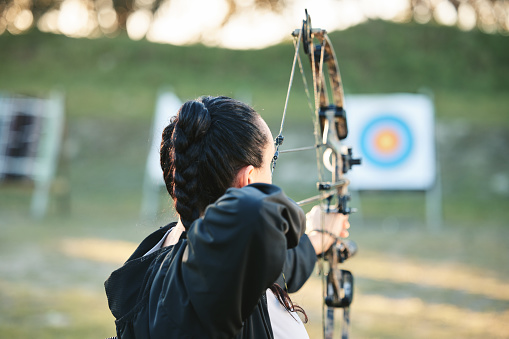 Archery, shooting range and target for sports training with a woman outdoor for bow practice. Archer athlete person with focus on field for competition or game to aim arrow for action and bullseye