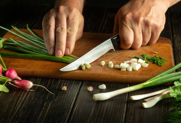 Chef hands cut fresh onion leaves on cutting board for vitamin salad. Diet menu in preparation for dinner in the kitchen
