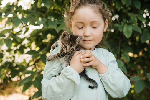 Child holding baby cat. Kids and pets. Little girl hugging cute little kitten in summer garden. Children with home pet animals