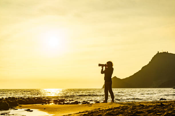 Silhouette of a lady taking a photo of a beautiful sunset with reflection of the sun in the cool calm water