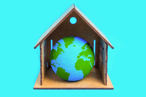 Tiny globe model nestled within a miniature wooden house isolated on blue. Sustainable living and harmonious coexistence with nature.