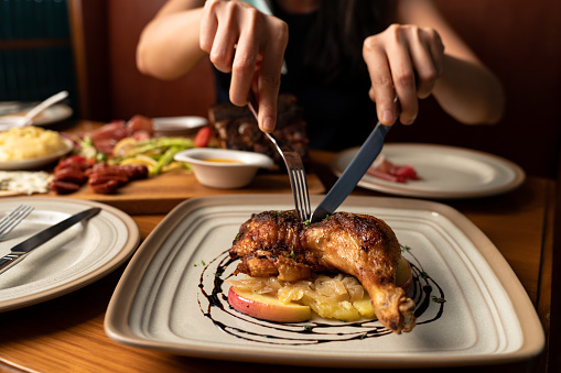 Person cutting grilled chicken on table of meal