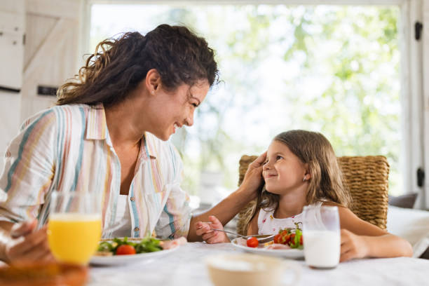 istock Loving mother and her small daughter talking while having breakfast at dining table. 1513087569