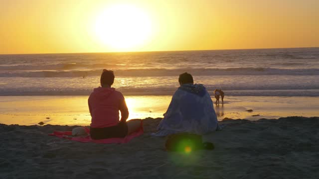 Couple Sitting on the Beach, Admiring the Sunset Over the Ocean in 4k slow motion 60fps