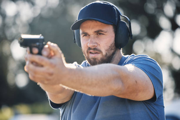 istock Man, gun and learning to aim at shooting range outdoor for security target training. Face of person train with safety gear headphones for focus on sport competition with firearm weapon in hands 1513104757