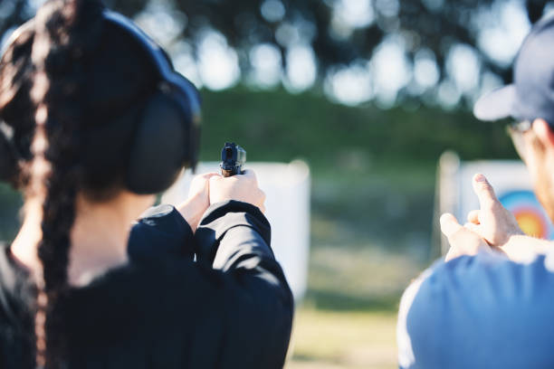 mujer, arma y aprendiendo a disparar al aire libre con instructor en el campo de tiro para el entrenamiento al blanco. seguridad y protección con la mano enseñando a la persona el juego deportivo o apuntar con equipo y arma de fuego para concentrarse - gun women handgun armed forces fotografías e imágenes de stock