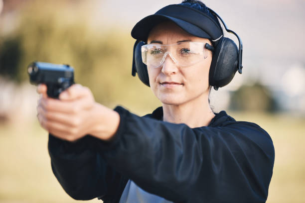 女性、銃、セキュリティ、訓練、ターゲットのために屋外の射撃場で武器を撃つことを学ぶ。スポーツ、競技、または安全のための安全ヘッドフォンと眼鏡を手にした人 - gun women handgun armed forces ストックフォトと画像