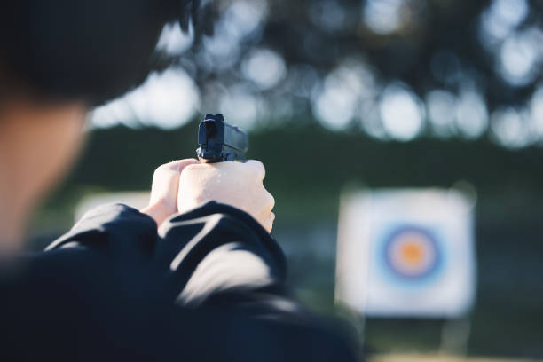 arma de fuego, blanco y persona entrenando al aire libre en el campo de tiro para ejercicios de juego o primer plano de desafíos deportivos. hombre manos con pistola, círculo y apuntar a la práctica, academia de policía o misión de práctica de campo - gun rounds fotografías e imágenes de stock