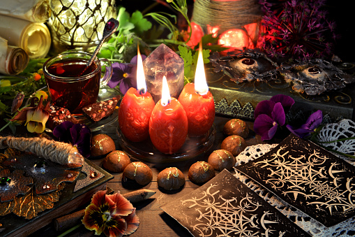 Still life with tarot cards, red candles, magic wand and book of spells on ritual table. Occult, esoteric and witchcraft concept. Mystic background with vintage objects