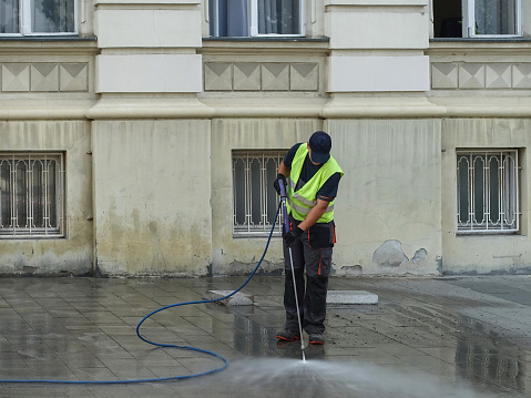 Novi Sad, July 3rd 2023. - Steam cleaning sidewalk with pressure, man with safety vest