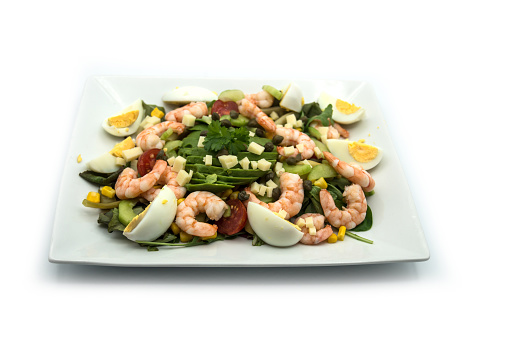 Closeup of avocado salade with shrimp in a white plate on white background