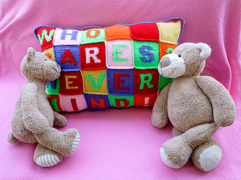 Two teddy bears lying on hand knitted pillow with colorful careless phrases