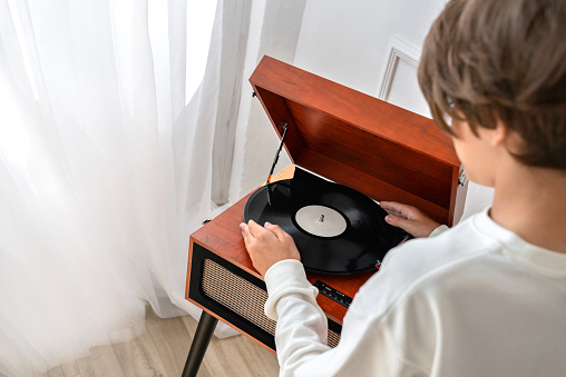 Teenager boy putting the vinyl record in a retro wooden brown turntable, player, music listening