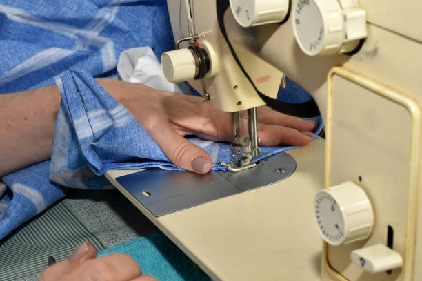 istock A seamstress works with a blue fabric behind a sewing machine. 1513281887
