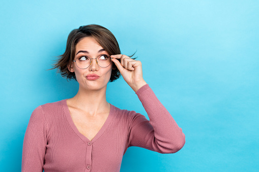 Photo of doubtful unsure lady wear pink cardigan hand arm spectacles looking empty space isolated blue color background.