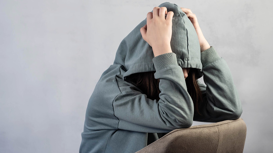 Teenage girl in depression, lonely thinks about problems and hides her face in a hood. The concept of adolescent psychology. Psychological problems.