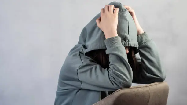 Teenage girl in depression, lonely thinks about problems and hides her face in a hood. The concept of adolescent psychology. Psychological problems.