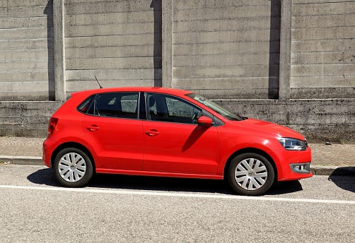 Udine, Italy. July 2, 2023. Red Volkswagen Polo under the sunlight on rough concrete wall background.