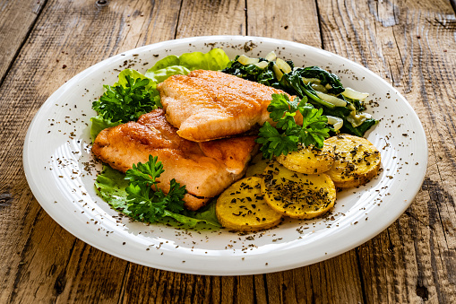 Seared salmon steaks, fried potatoes and spinach on wooden background