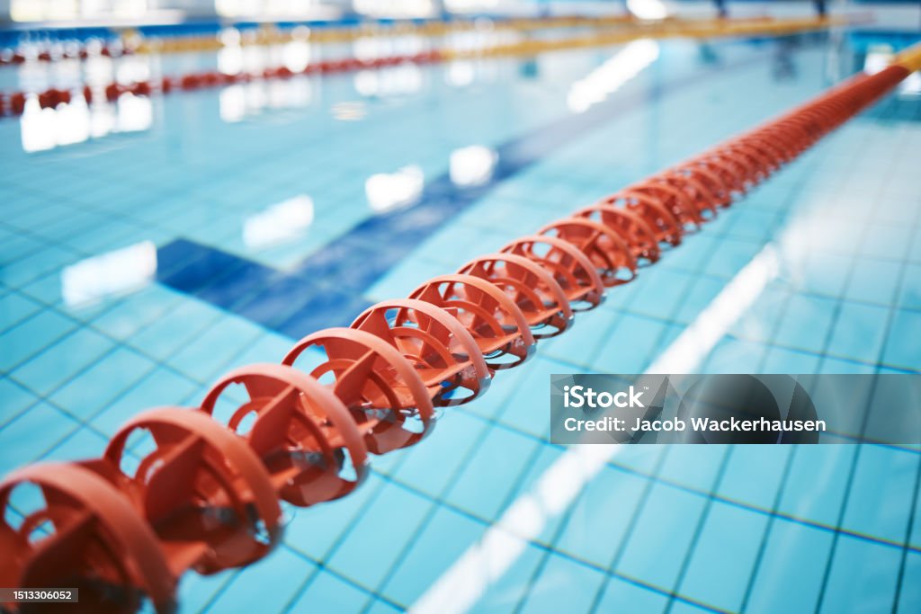 Water, empty swimming pool and lanes for competition, exercise and workout. Sports, swim and fitness with lane ropes or divider in liquid for aquatic training, exercising or underwater practice. Indoors Stock Photo