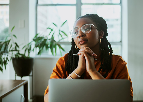 black business woman sitting and thinking at her desk wearing orange.