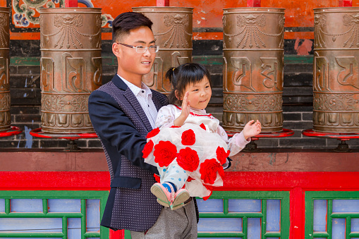 A dad and a young girl pose in front of aniken prayer wheels of a temple in Kumbum Jampaling monastery complex, Xining, China, May 14th, 2015