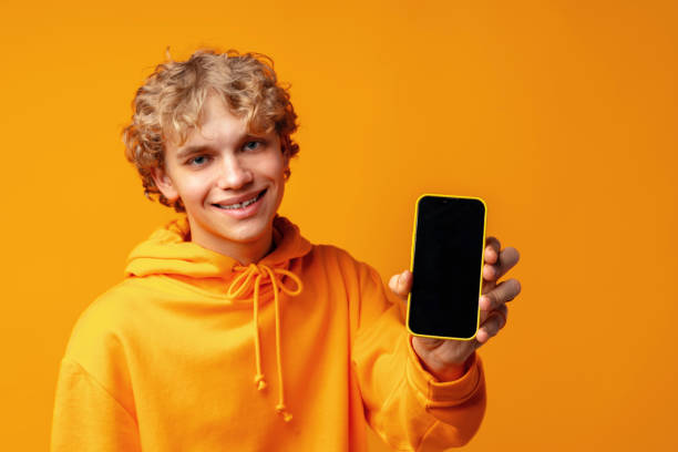 istock Young smiling man holding smartphone with blank device screen against yellow background 1513373422
