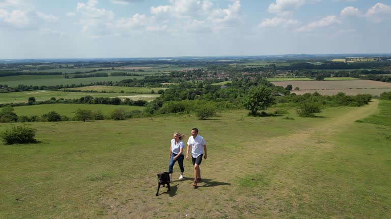 Drone Shot Of Mature Couple Walking With Pet Dog Through Beautiful English Countryside In Oxfordshire England UK