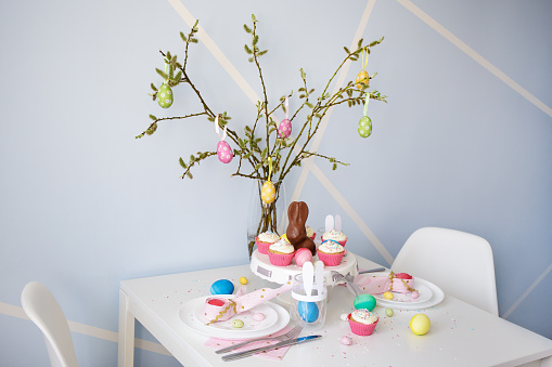 spring, holidays and easter concept - decorated table with pussy willow branch, cupcakes, colorful painted eggs and bunnies