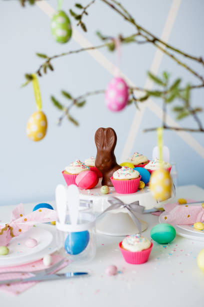 Ozdoby wielkanocne - udekorowany stół z babeczkami, kolorowymi malowanymi jajkami i czekoladowym zajączkiem – zdjęcie