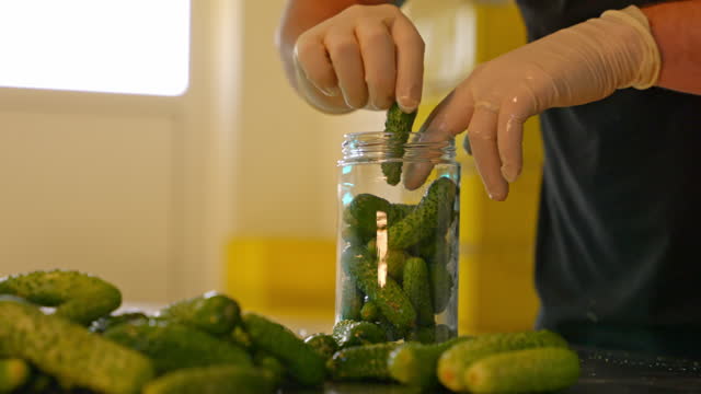 SLO MO Hands in Gloves Filling a Jar with Cucumbers, Preparing them for Pickle Perfection