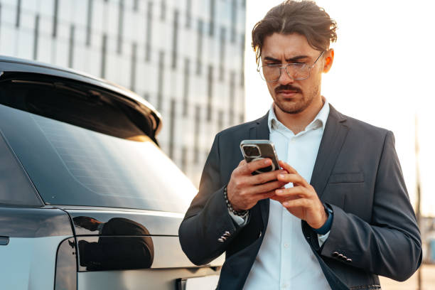 istock Young businessman standing near luxury car and using smartphone 1513436599